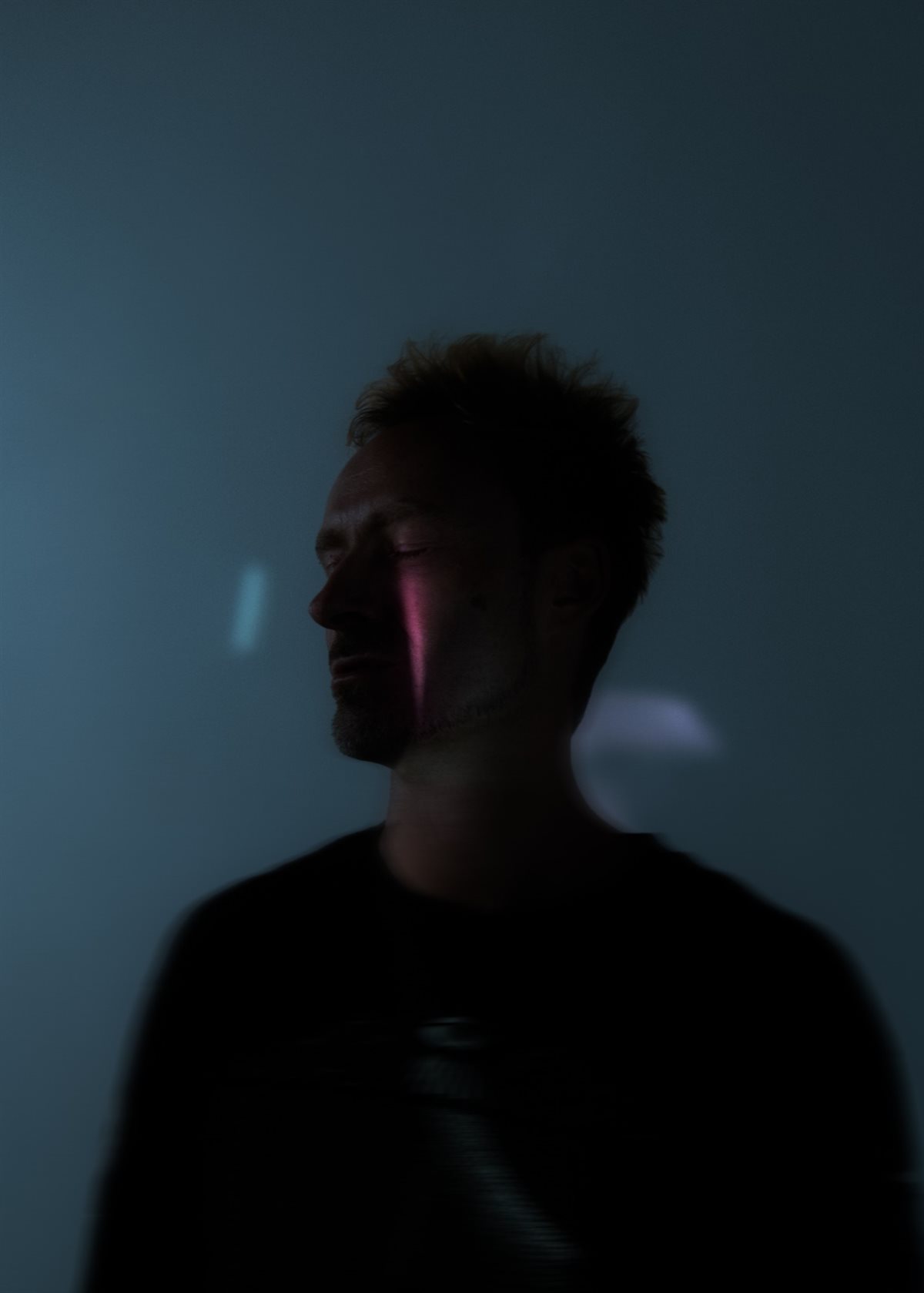 Robot Koch, eyes closed, in a dark blue room with a streak of pink light across his face.